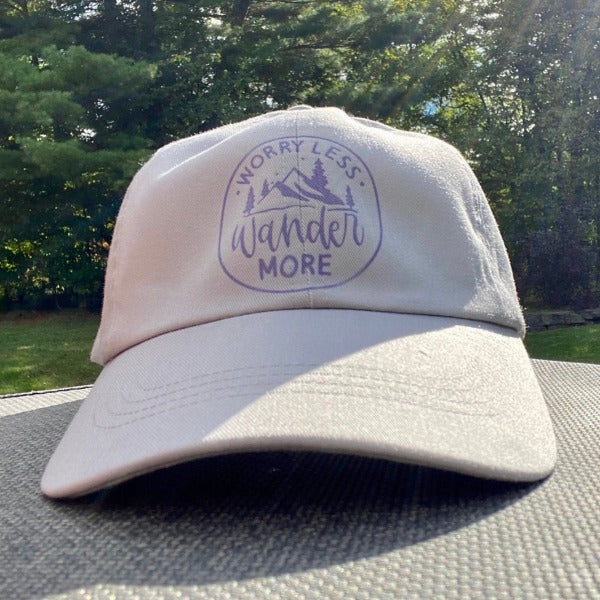 Another Glamping Essential - the 'Worry Less Wander More' ball cap. Printing is in purple, ball cap is grey.