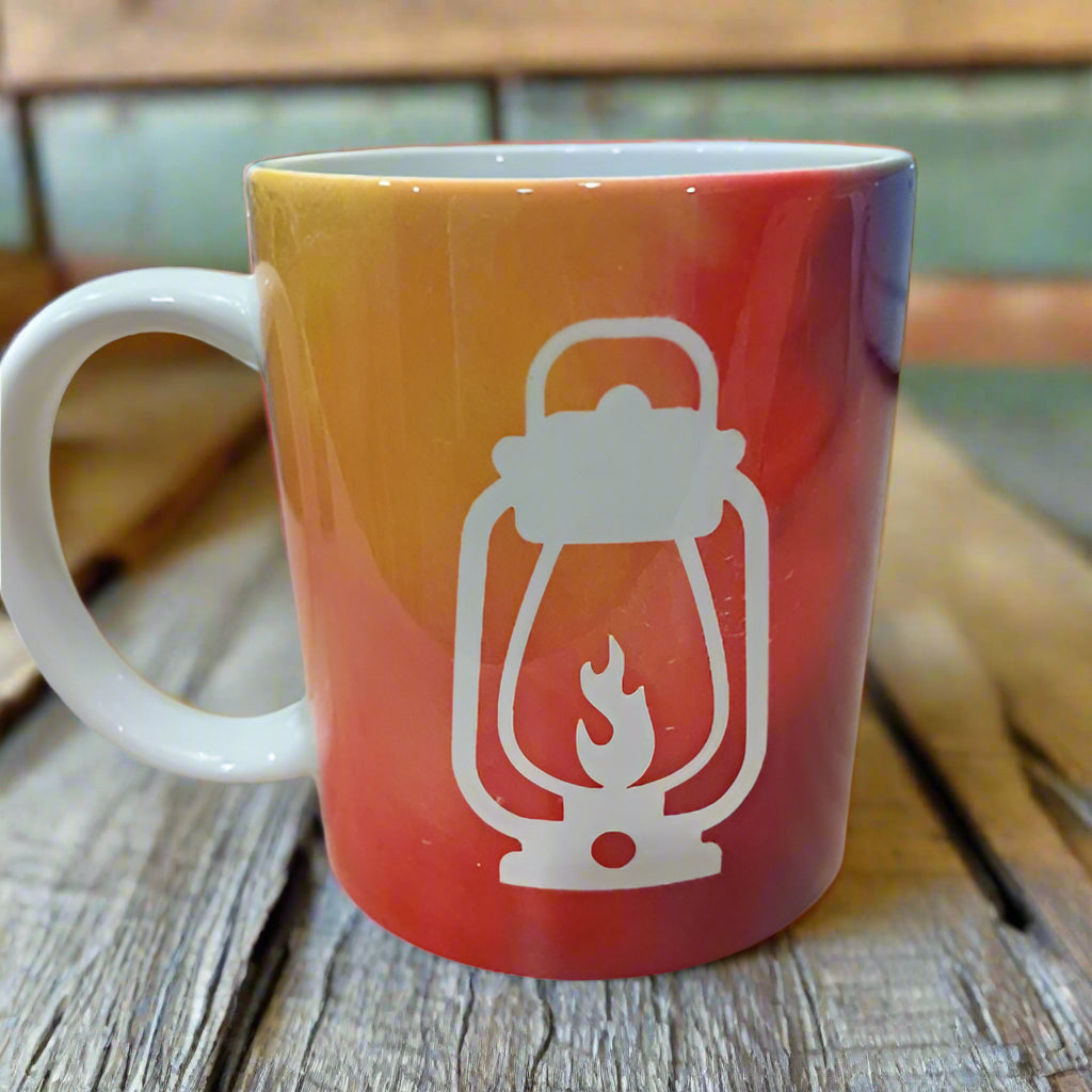 The back of the Happy Glamper mug shows a white camping lantern on a background of orange and red tie-dye.