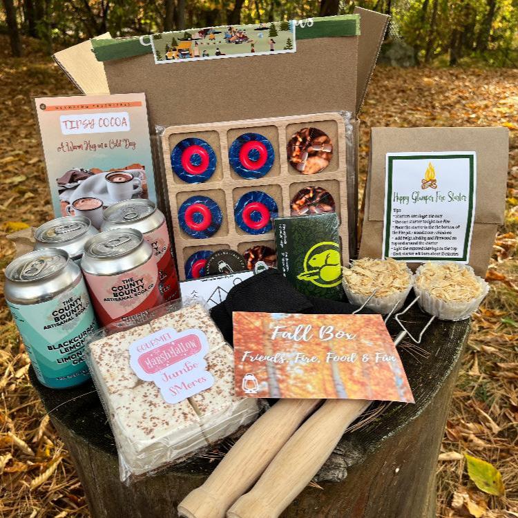 All the items from the Fall 2023 Glamping Box: soda, smores marshmallows, roasting sticks, playing cards, fire starters and tic tac toe