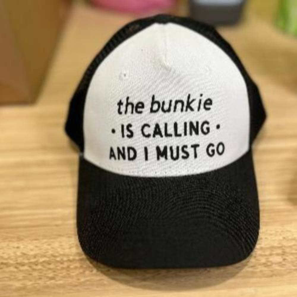 Black trucker back cap with white front, says "the bunkie is calling and I must go"