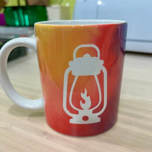 The back of the Happy Glamper mug shows a white camping lantern on a background of orange and red tie-dye.
