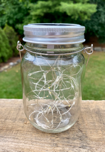 Solar lantern made from a mason jar and fairy lights.  It has a silver lid and thin metal band to hand it from a tree, clothesline or whatever you need to hang it from.  A true Glamping essential.