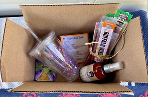 The complete June Glamping Box - Basecamp cards, 'Life is Better in Flip Flops' tumbler, Slushi drink recipe, packages of pepperoni sticks and 'Bug Off' natural bug repellent, all in a cardboard box.