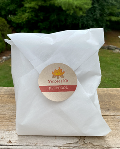 Our s'mores kit from the August Glamping Essential's Box. Behind the white, wax paper, is a kit including delicious chocolate dipped graham crackers and hand-made marshmallows. This kit was included the August Glamping Essential's Box and is sure to be a hit!