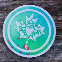 Round ceramic coasters, 100% customizable. This one has a mosaic of hearts making up a maple leaf in white over a green/blue tie-dye background.